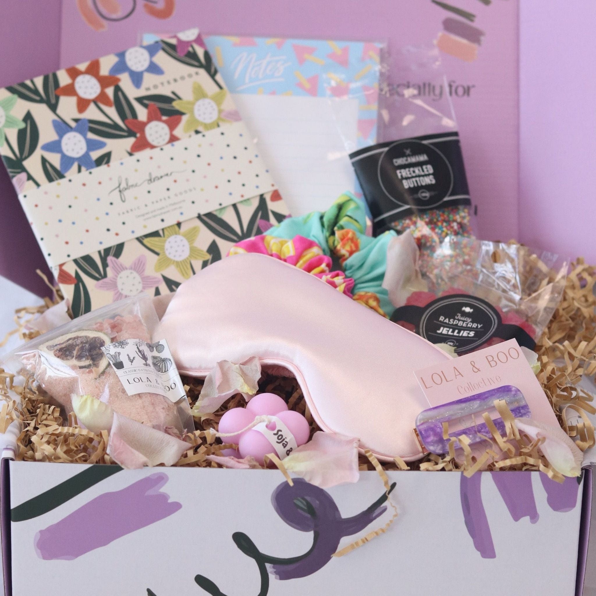 gift box filled with silk eye mask, hair clips, chocolate, candy, bath salt, book, note pad.