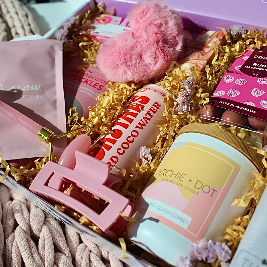 Beaut Box with Pamper & Self-Care Products for Women including a soap, chocolate bag, candle, hair claw, keychain, face mask, face roller, coconut water, bag, and rocky road treat