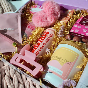 Beaut Box with Pamper & Self-Care Products for Women including a soap, chocolate bag, candle, hair claw, keychain, face mask, face roller, coconut water, bag, and rocky road treat