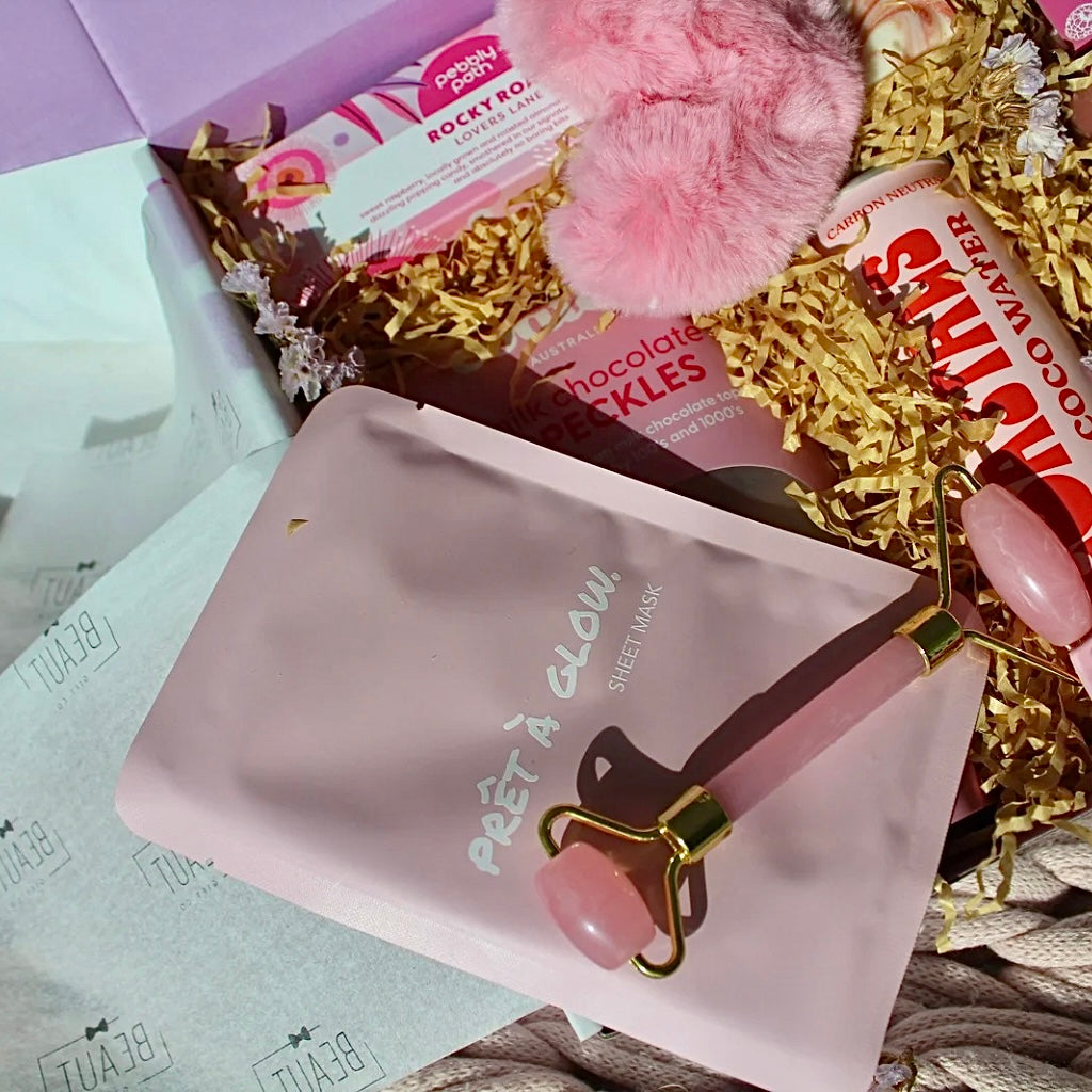 Beaut Box with Pamper & Self-Care Products for Women including a soap, chocolate bag, candle, hair claw, keychain, face mask, face roller, coconut water, bag, and rocky road treat