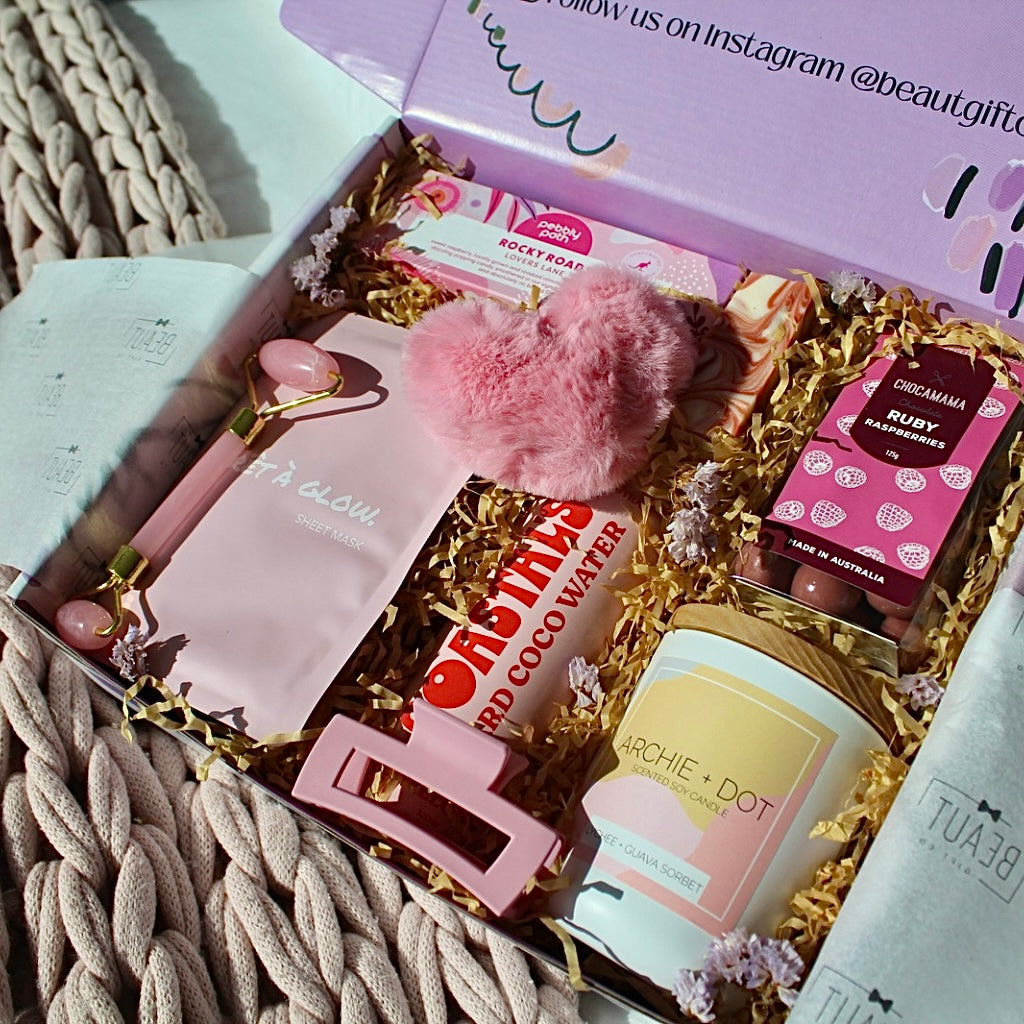 Beaut Box with Pamper & Self-Care Products for Women including a soap, chocolate bag, candle, hair claw, keychain, face mask, face roller, coconut water, bag, and rocky road treat